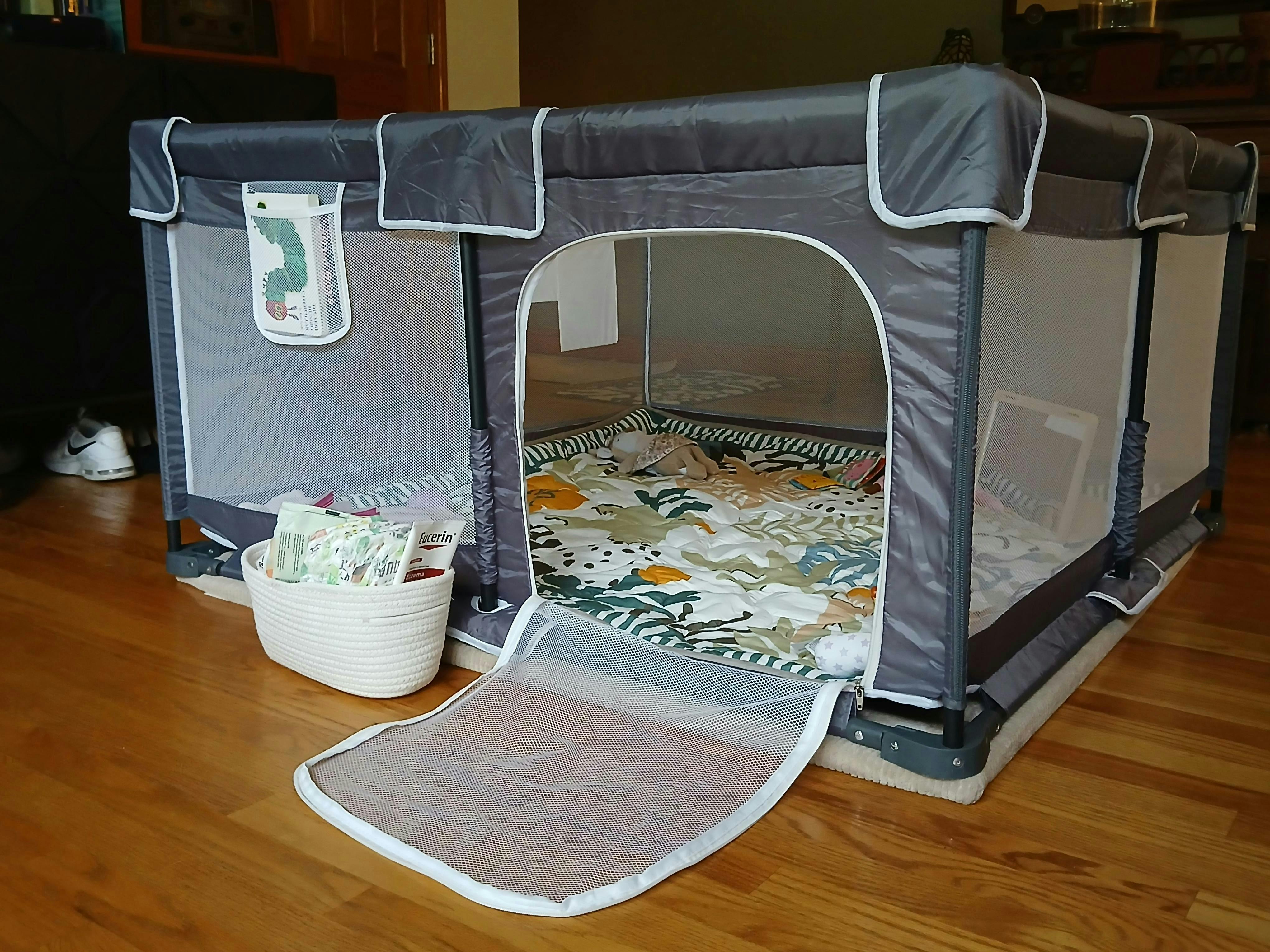Playpen with a patterned mat and a storage basket on a hardwood floor