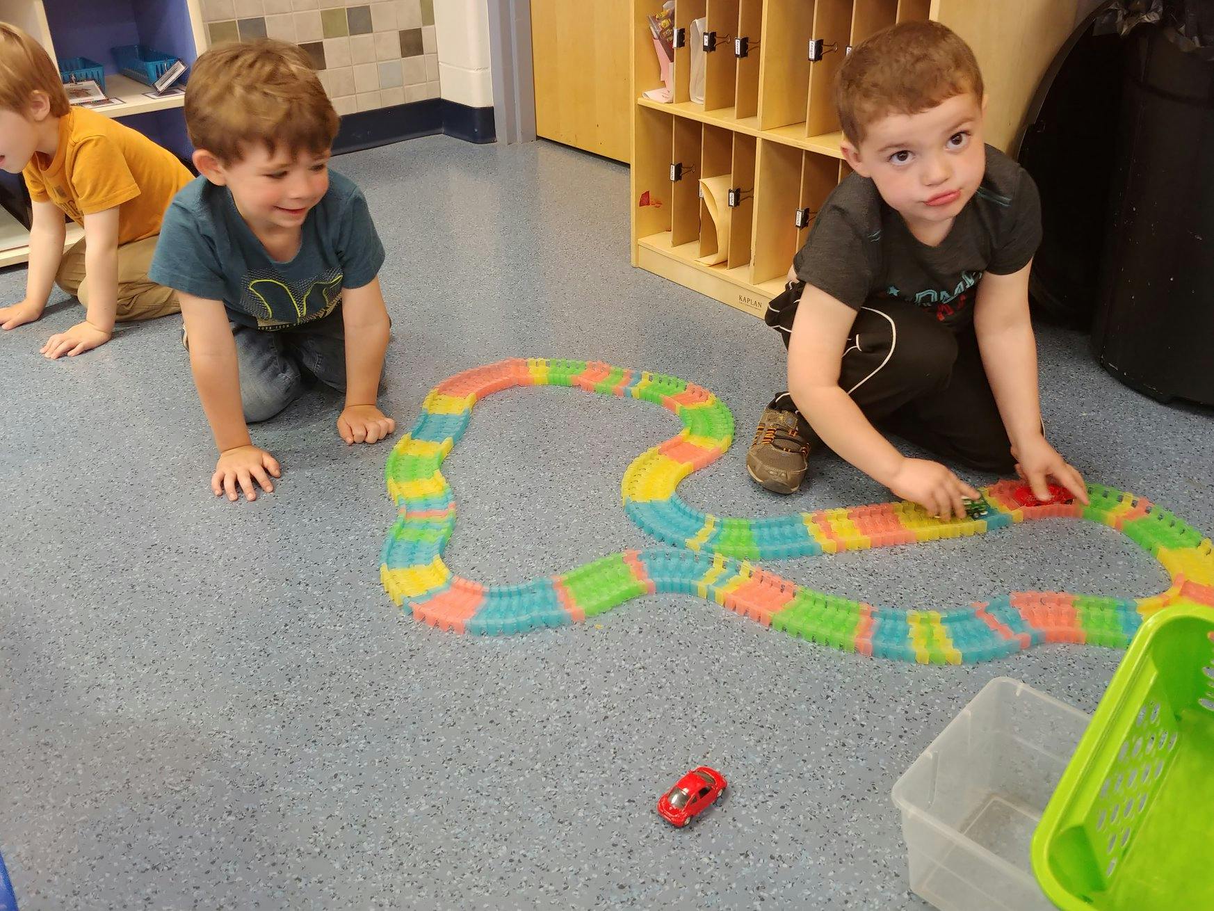 Two children playing with a colorful toy car track on the floor
