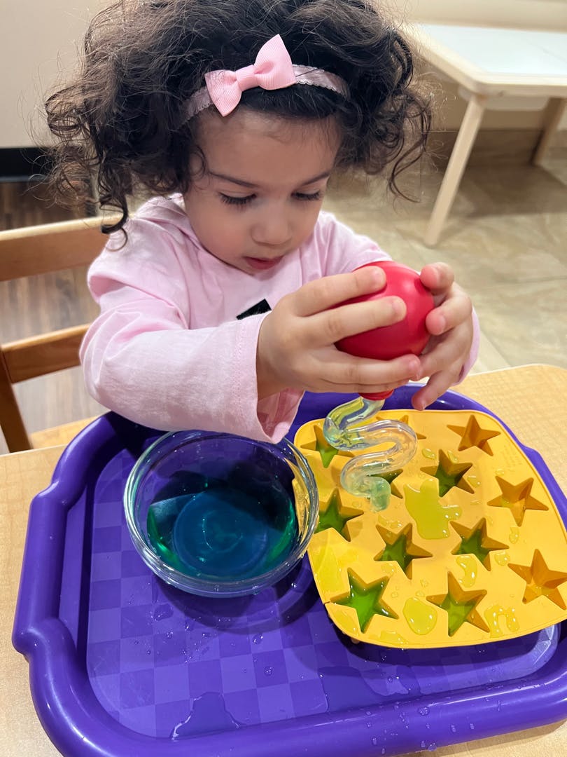 Child using a red bulb syringe to transfer liquid into a star-shaped mold