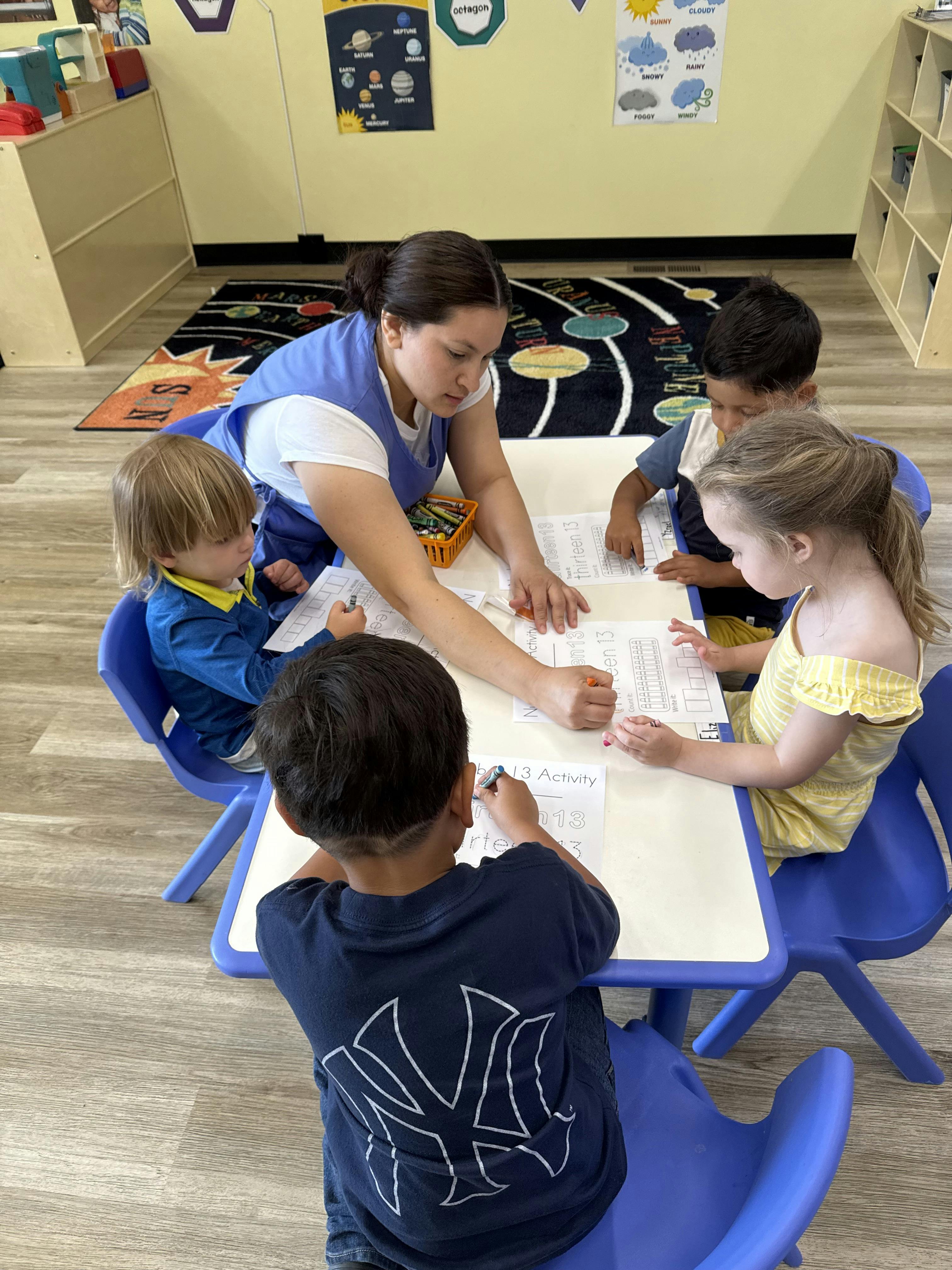 Teacher and children working on worksheets at a classroom table