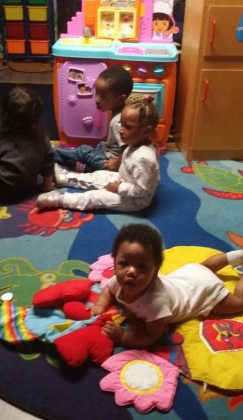 Three children on a colorful rug, one child on their stomach looking forward