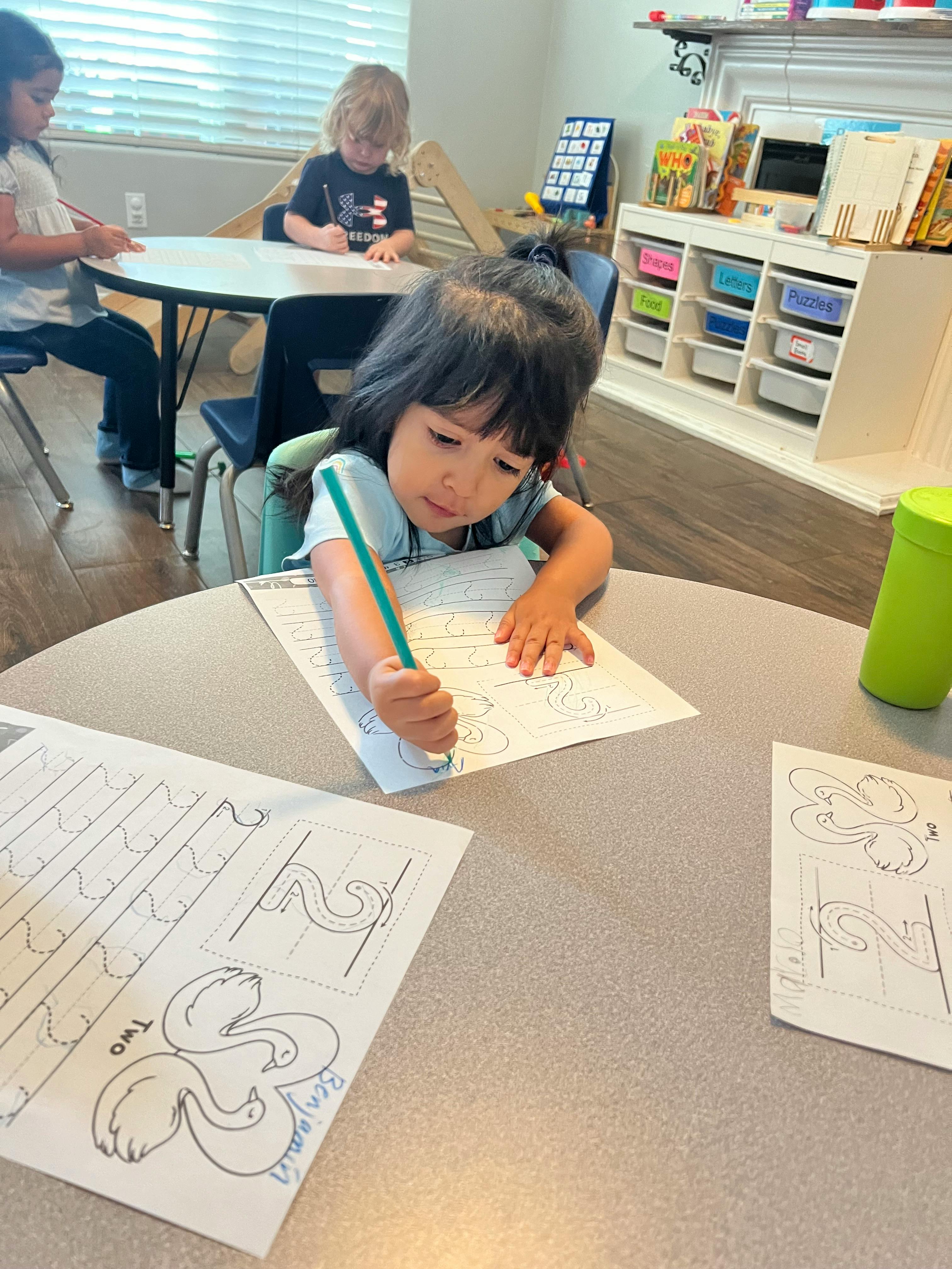 Child writing on paper at a table in a classroom