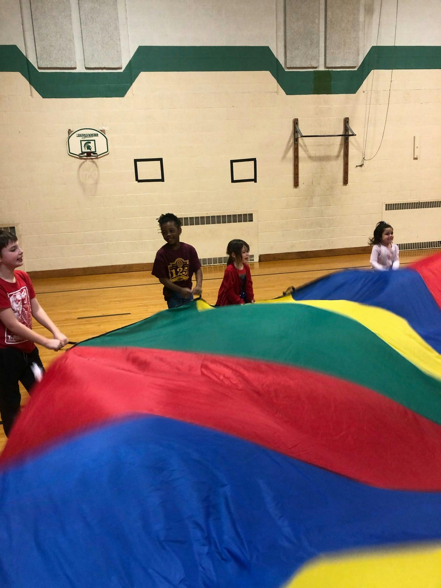 Children playing with a large colorful parachute in a gymnasium