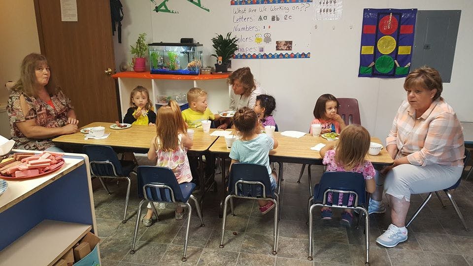 Adults and children sitting at tables in a classroom