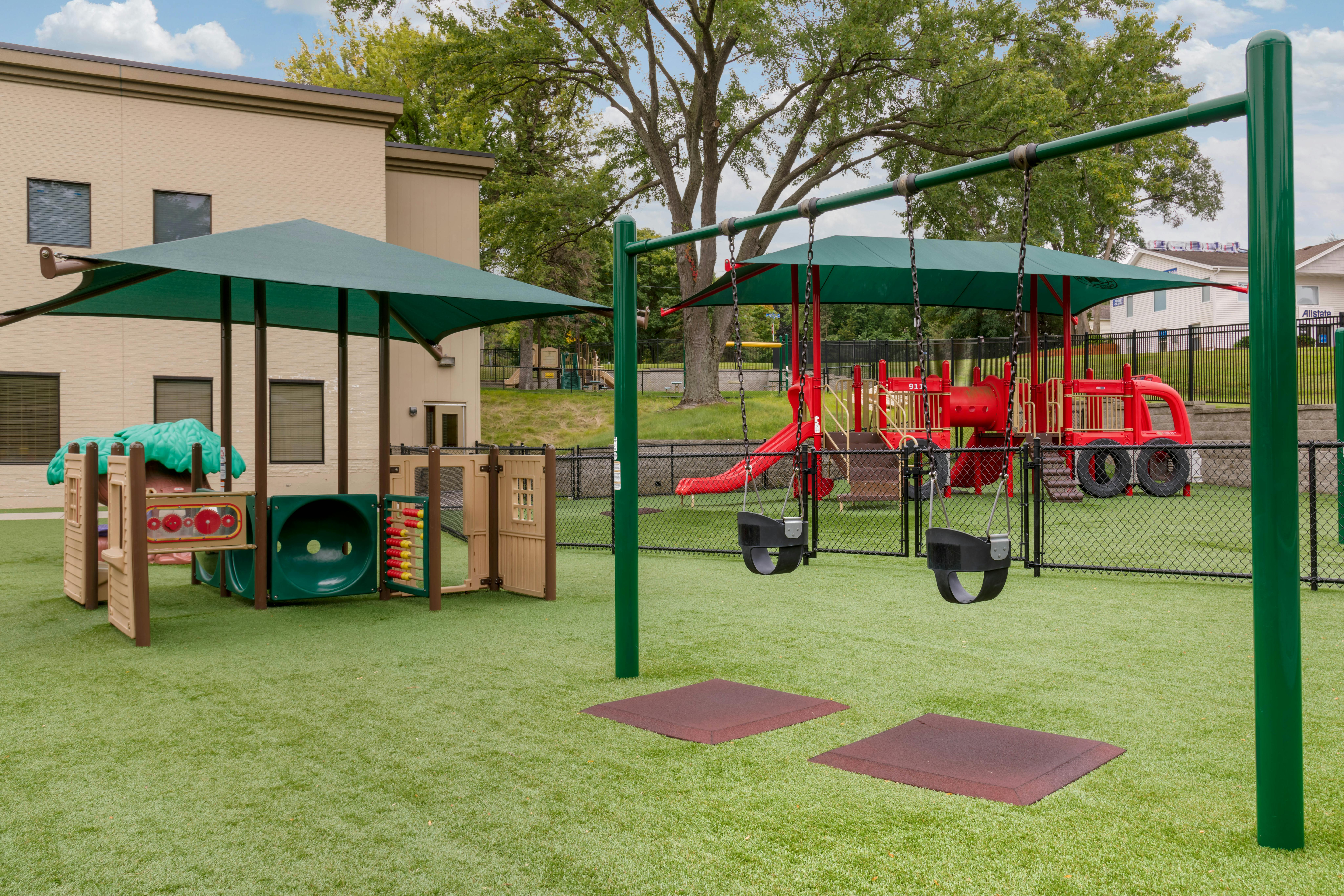 Playground with green turf, swing sets, and play structures under shade canopies