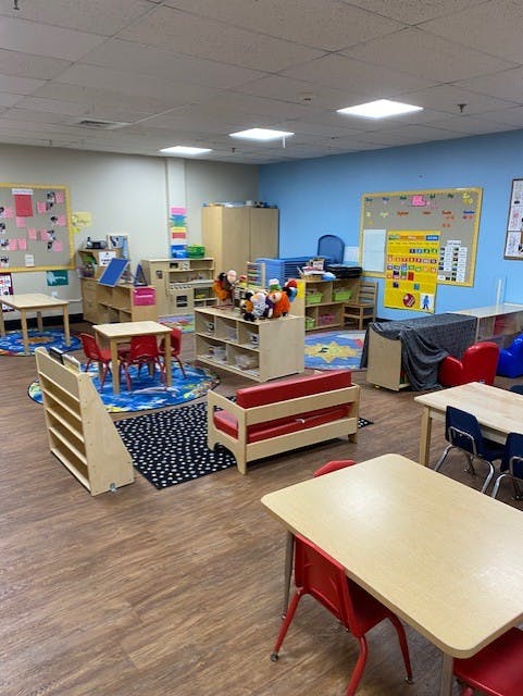 Children's classroom with small tables, chairs, rugs, and shelves with toys