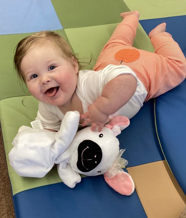 Child lying on a colorful mat playing with a stuffed toy
