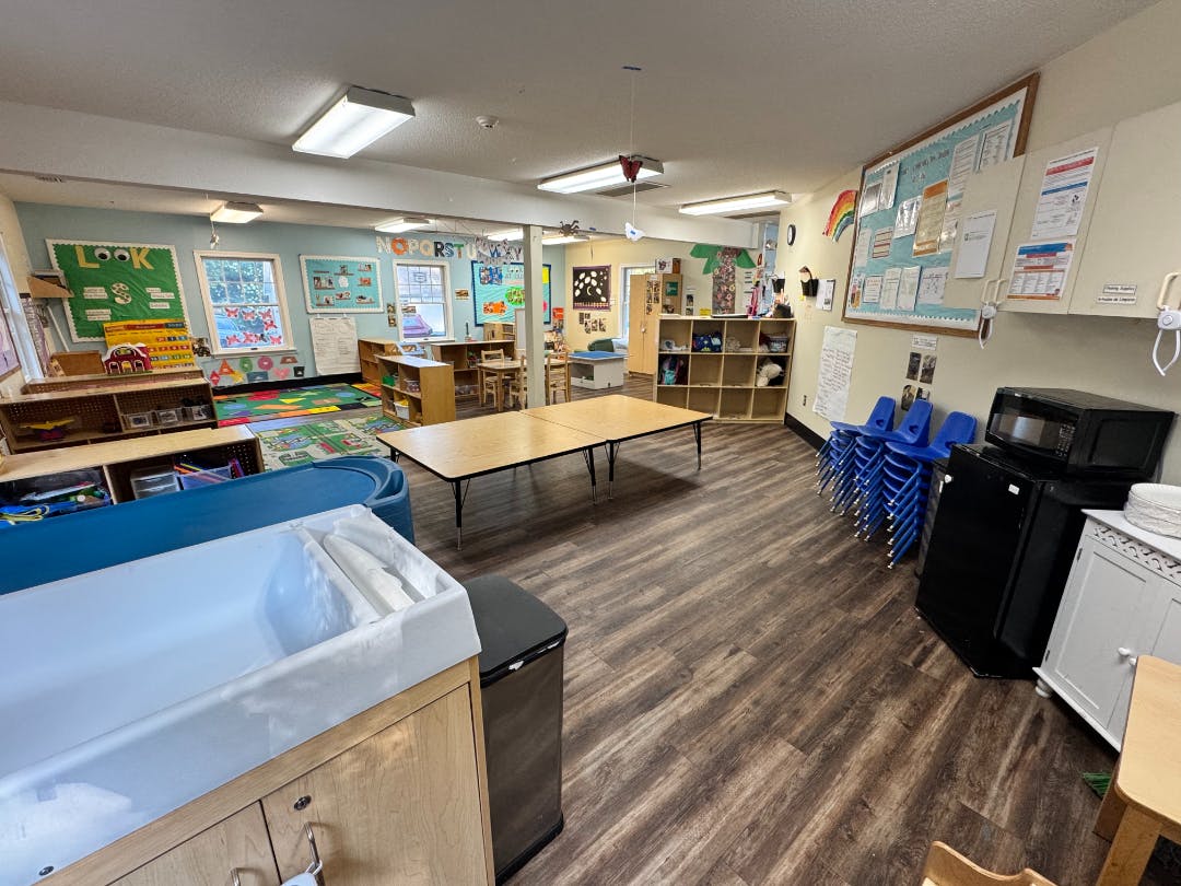 An empty childcare classroom with small tables, chairs, and learning materials