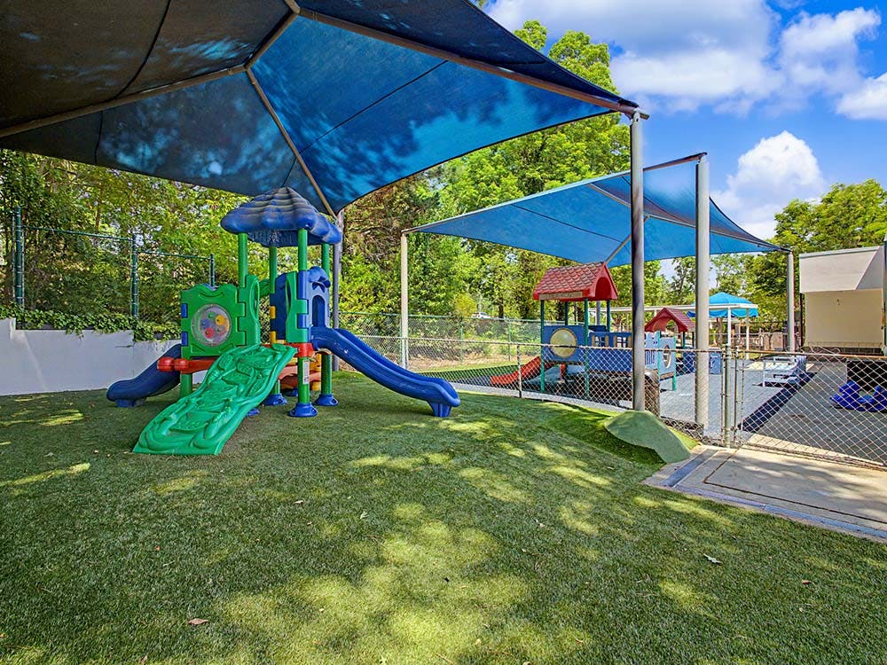 Playground with blue canopy shades over artificial turf