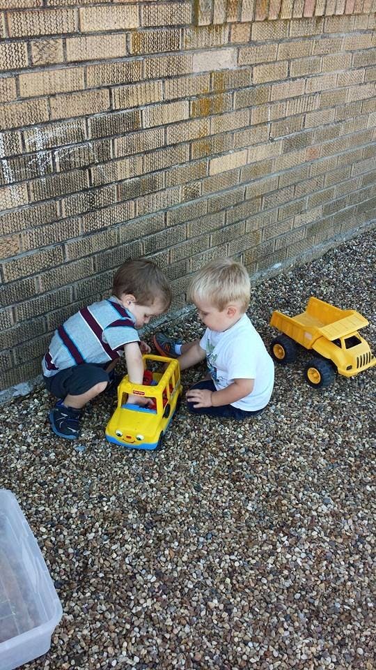 Two children playing with toy trucks on a gravel surface