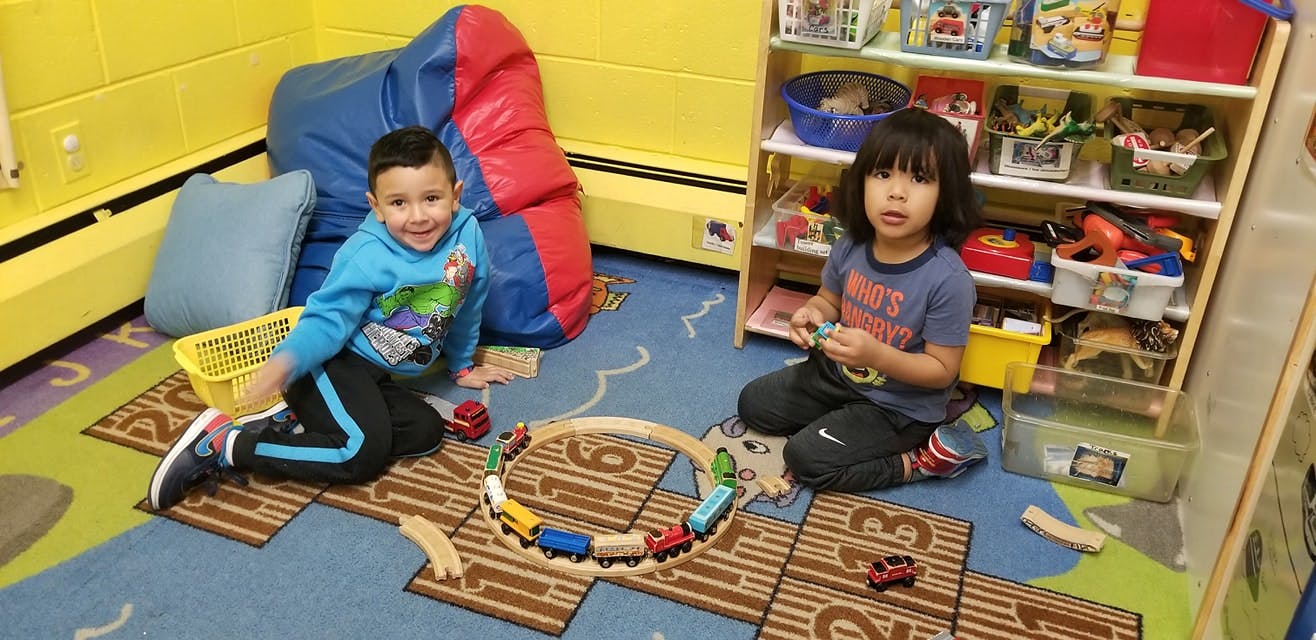 Two children playing with a toy train set on the floor