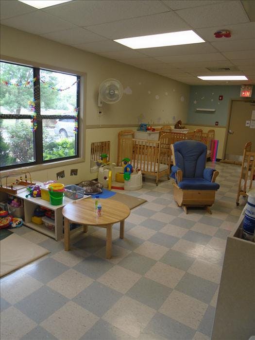Empty nursery room with multiple cribs, a rocking chair, and a small table
