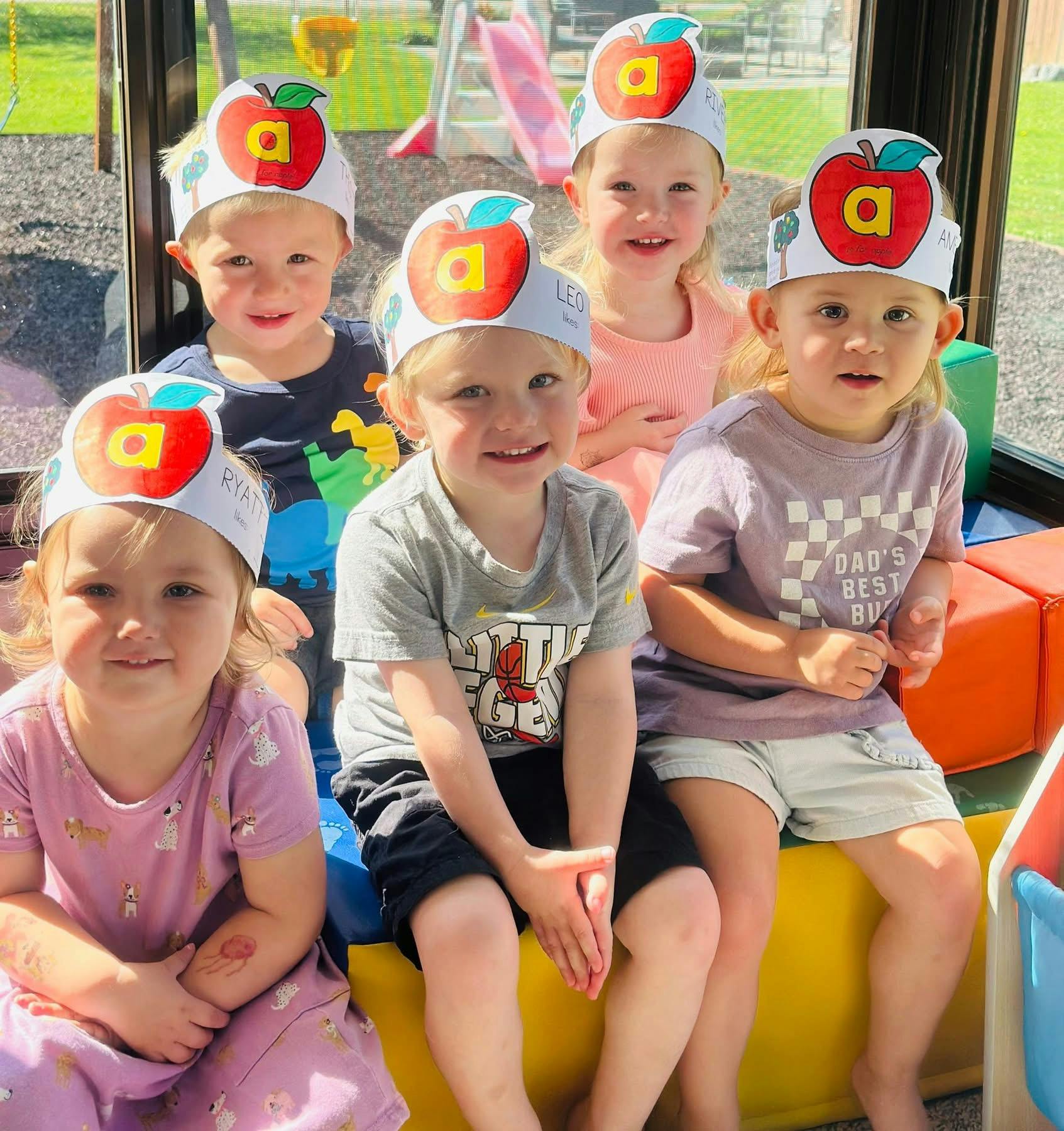 Five children wearing paper apple crowns with the letter A