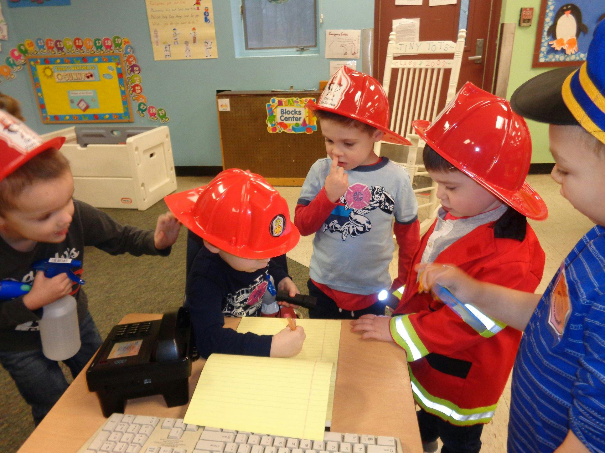 Children in firefighter hats and costumes playing in a classroom