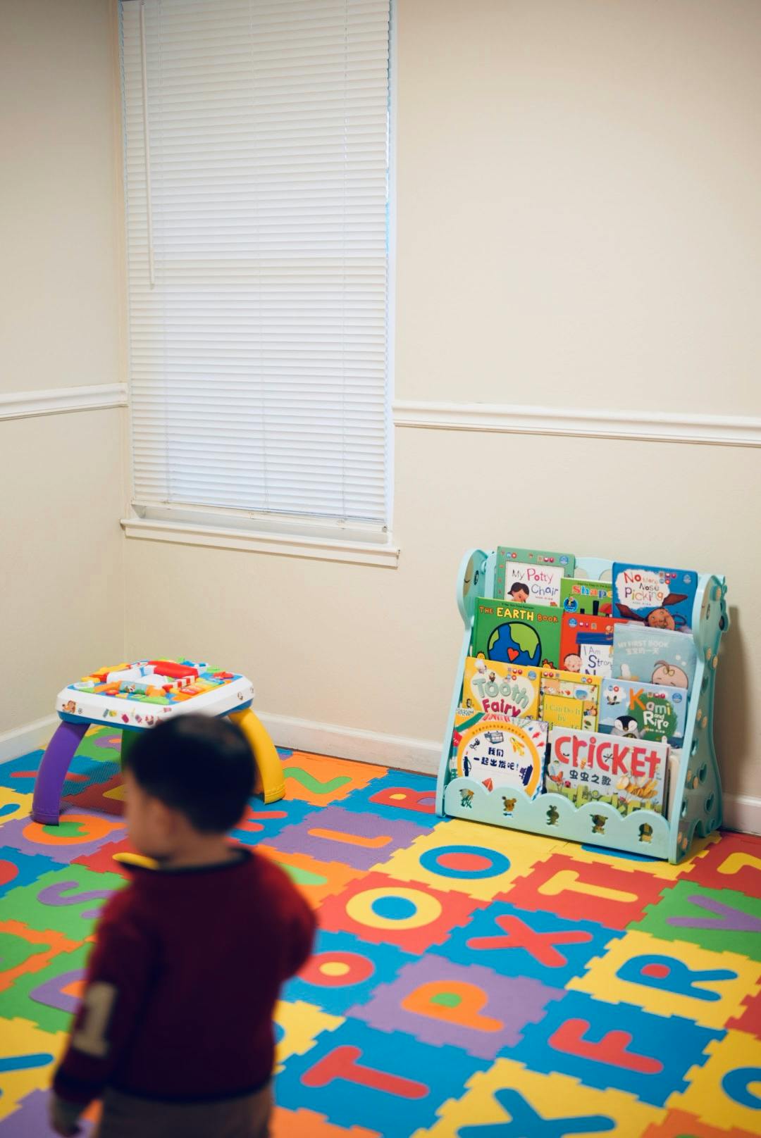 Child standing on alphabet playmat in a room with a book display