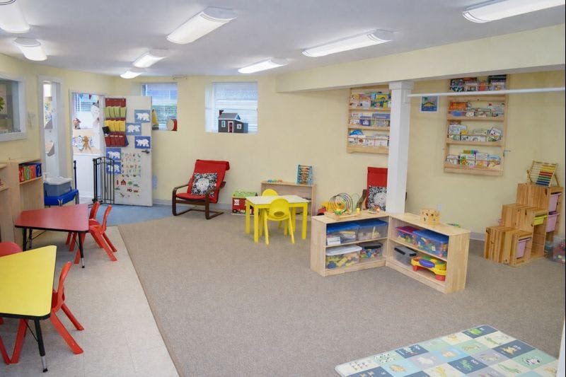 A playroom with small tables and chairs, shelves with toys, and wall-mounted book displays