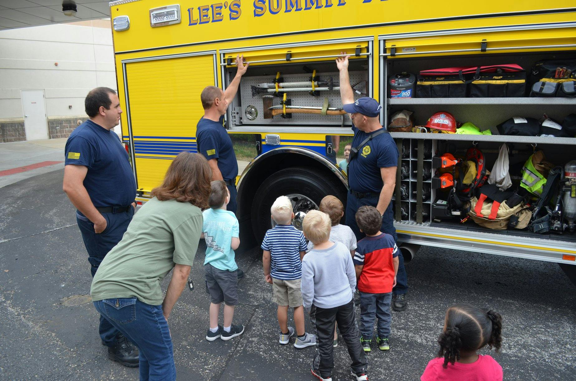 People and children gathered around a fire truck with open compartments