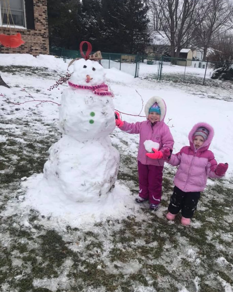 Two children standing next to a snowman