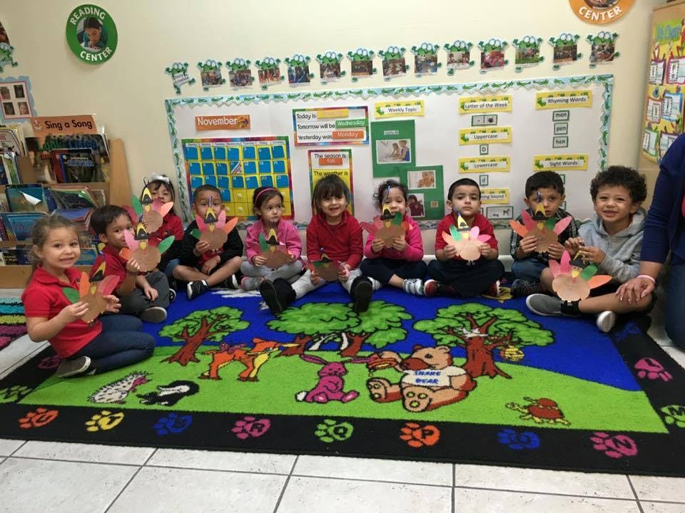 Children sitting on a rug holding paper crafts