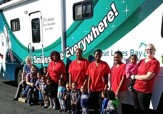 Adults and children standing in front of a mobile dental clinic