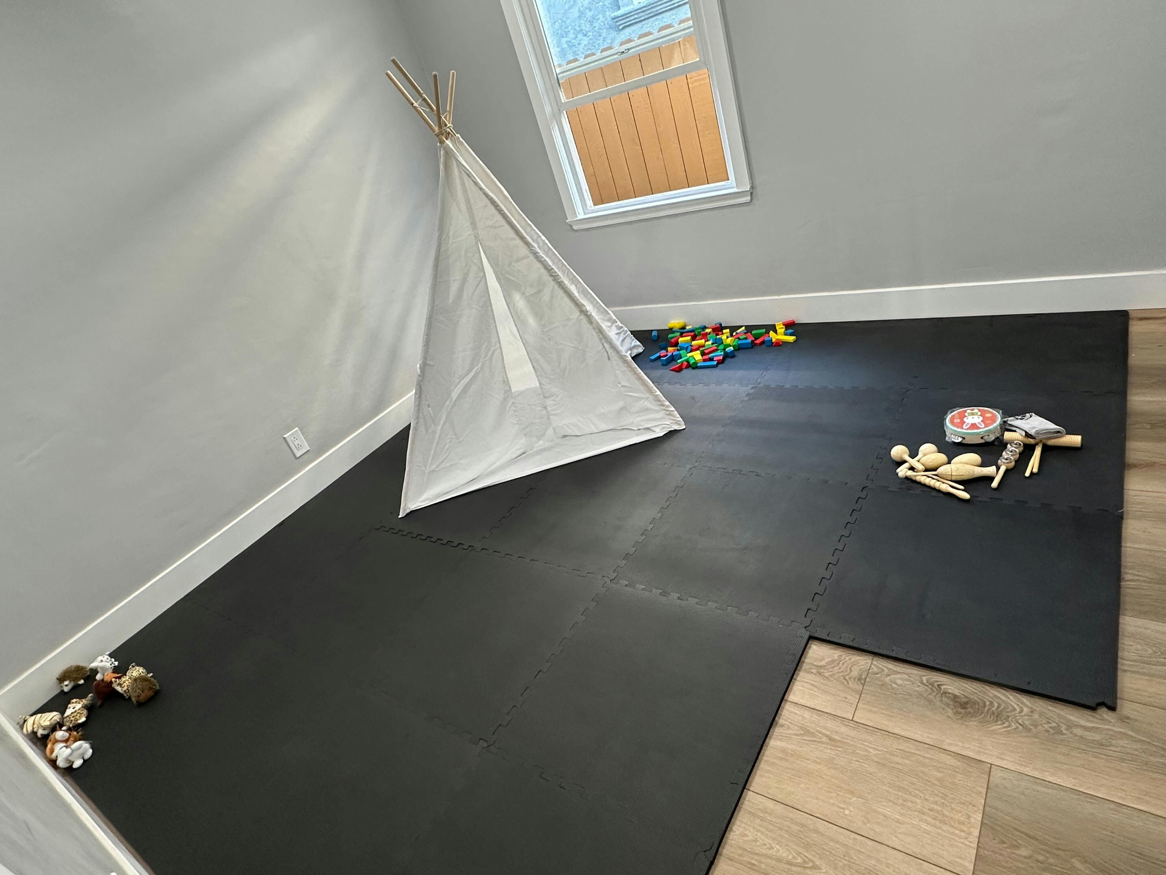 Playroom with a white teepee, toys, and a black mat on the floor
