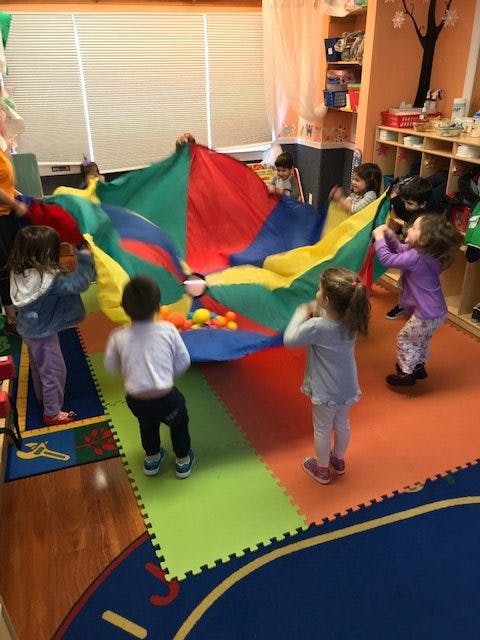 Children playing with a colorful parachute and balls in a classroom