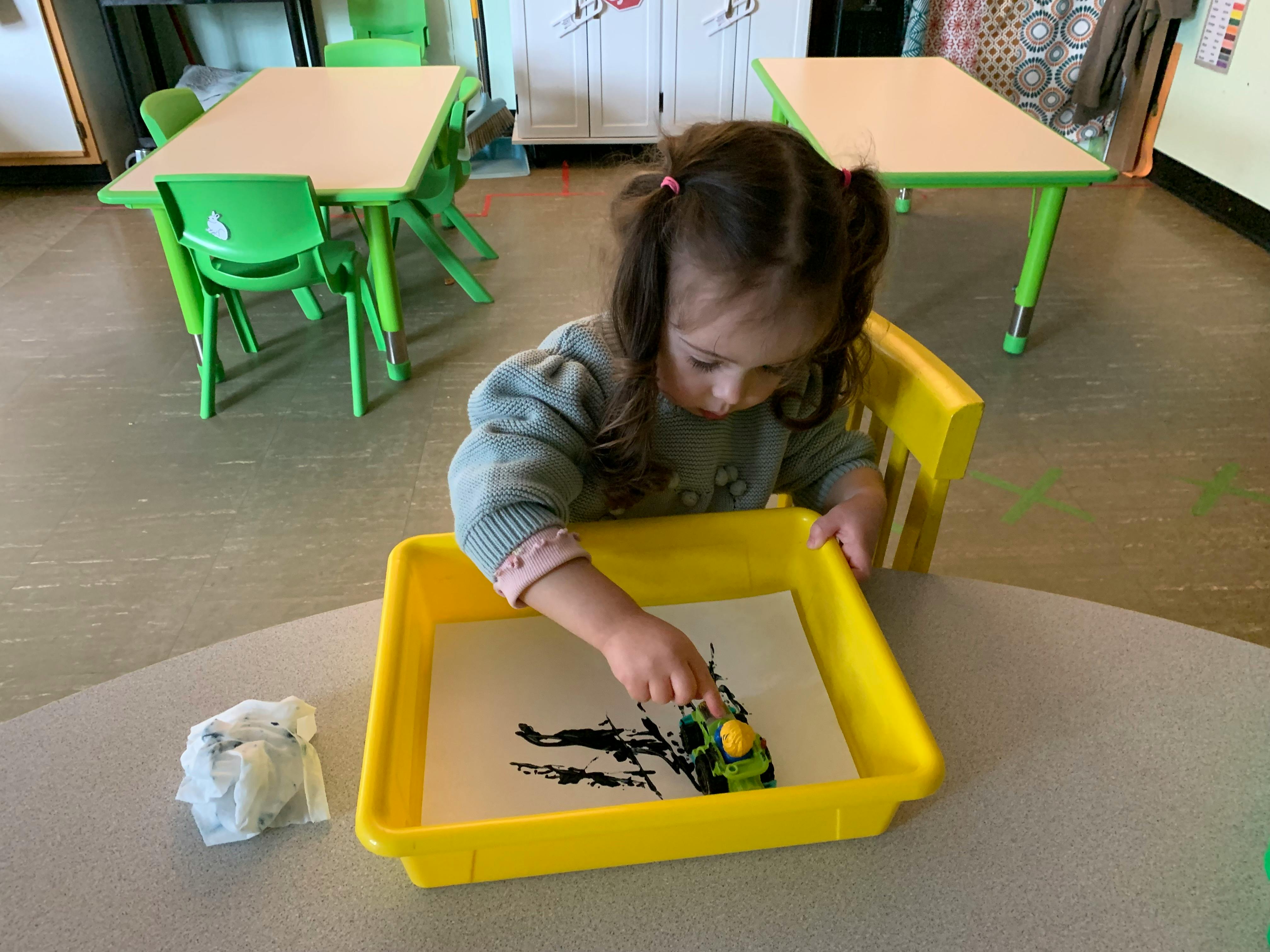 Child playing with a toy car and black paint in a classroom