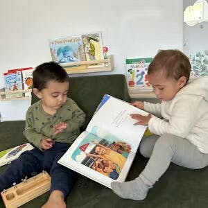 Two children sitting on a couch reading a book together