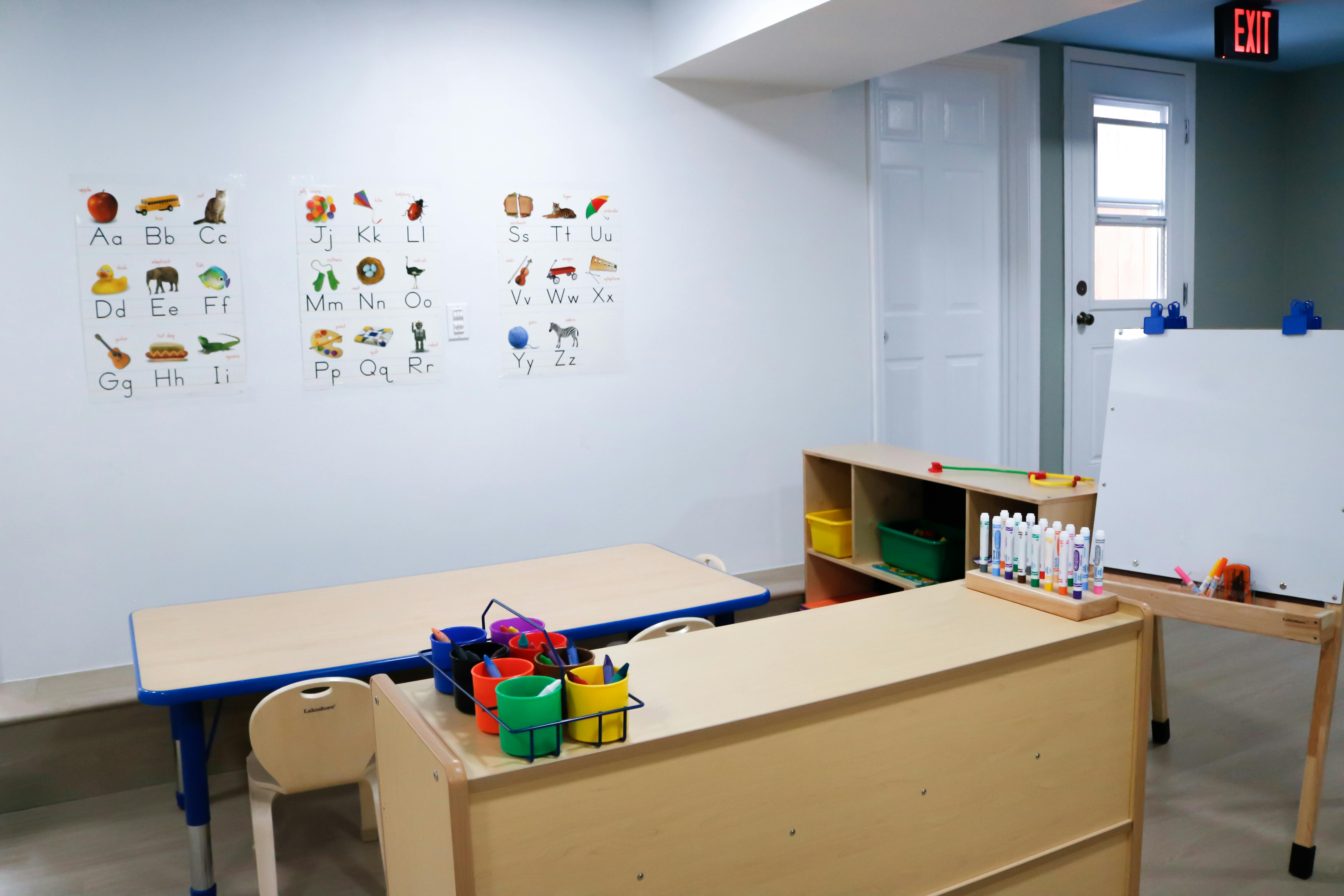 Classroom with ABC posters, tables, chairs, art supplies, and an exit sign