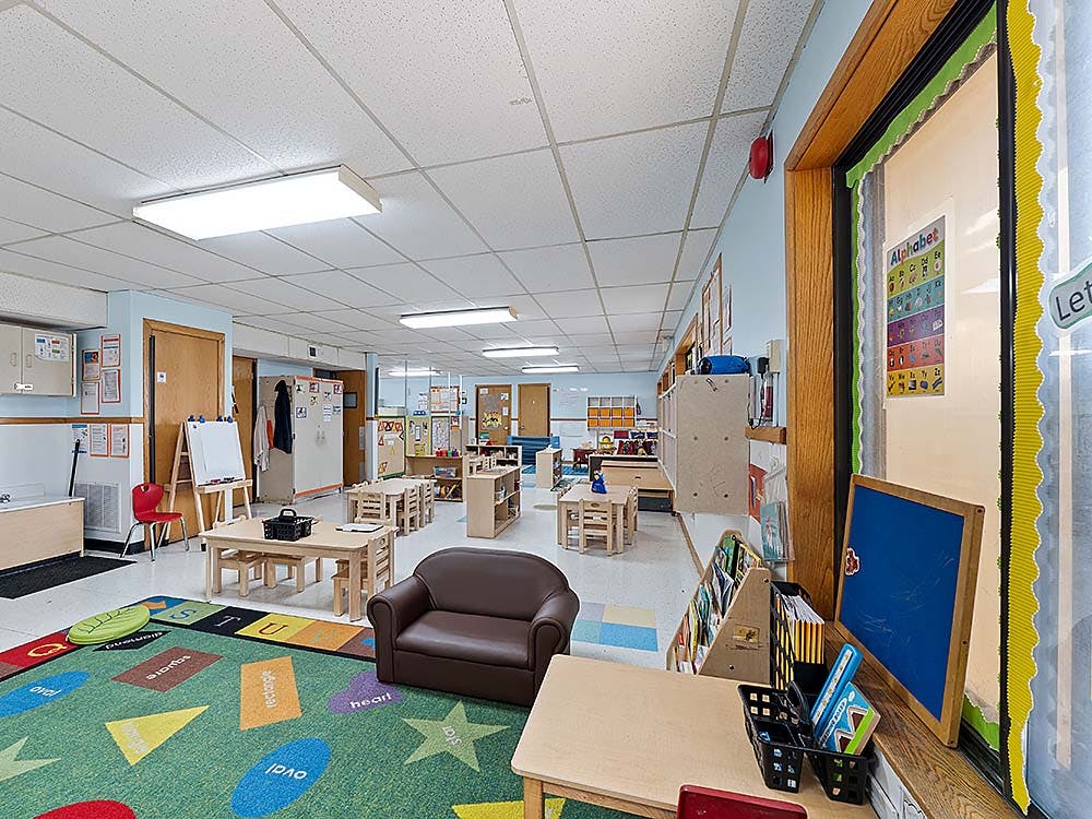 Classroom with small tables, chairs, and a colorful rug with shapes