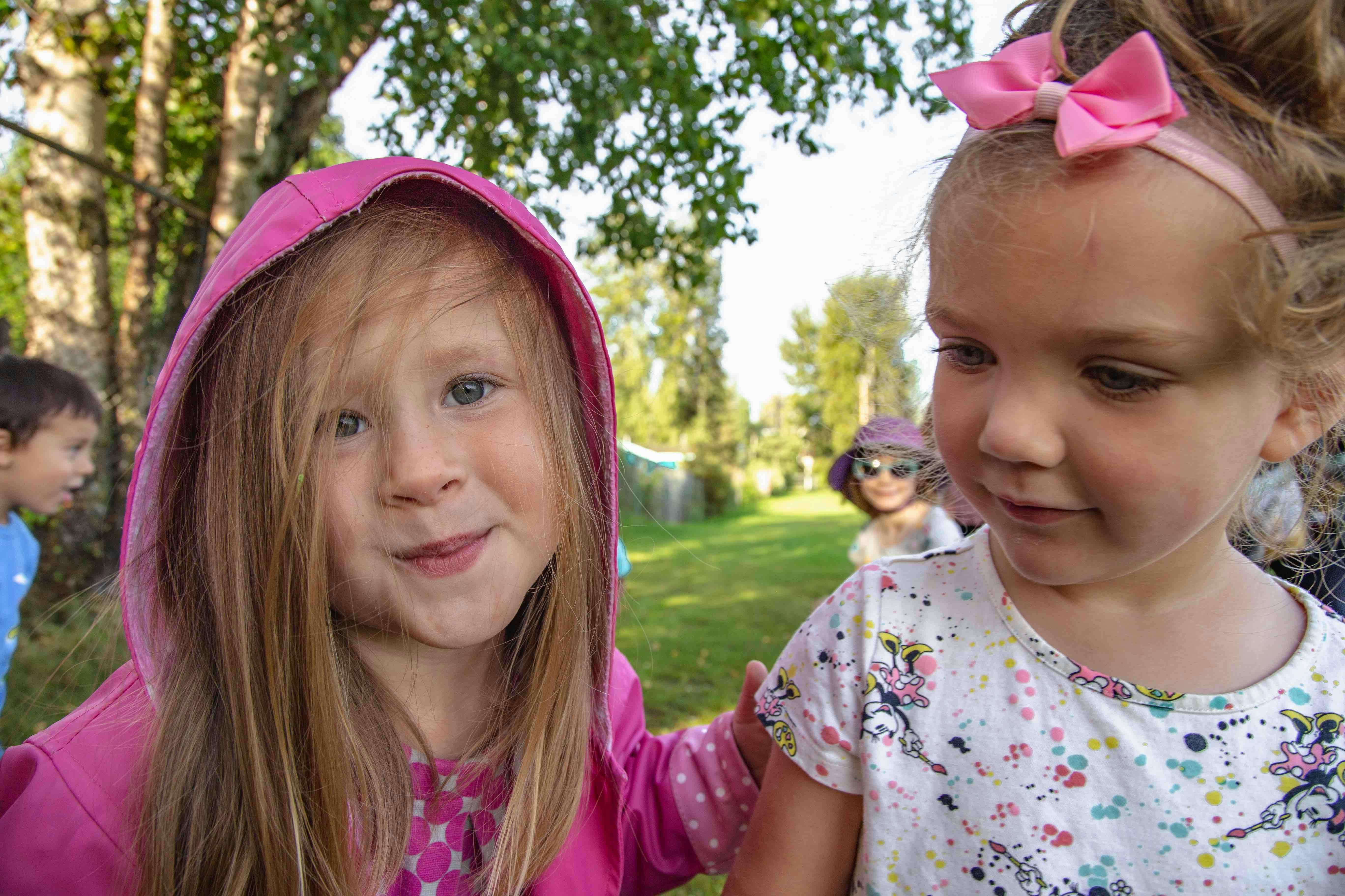 Two children outdoors, one in a pink hooded top, one in a white top