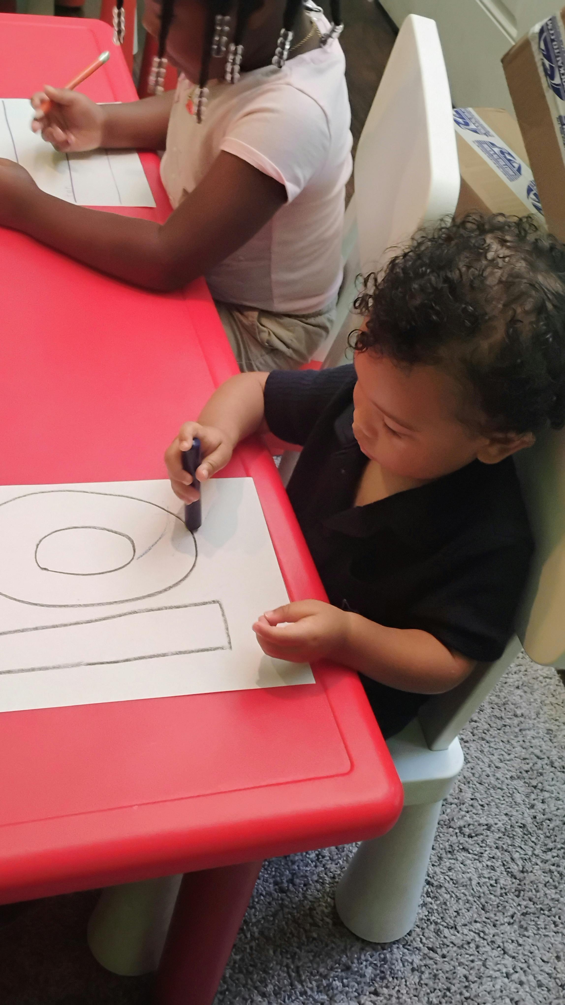 Two children sitting at a red table drawing on paper