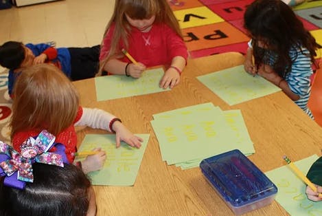 Children writing on paper at a table