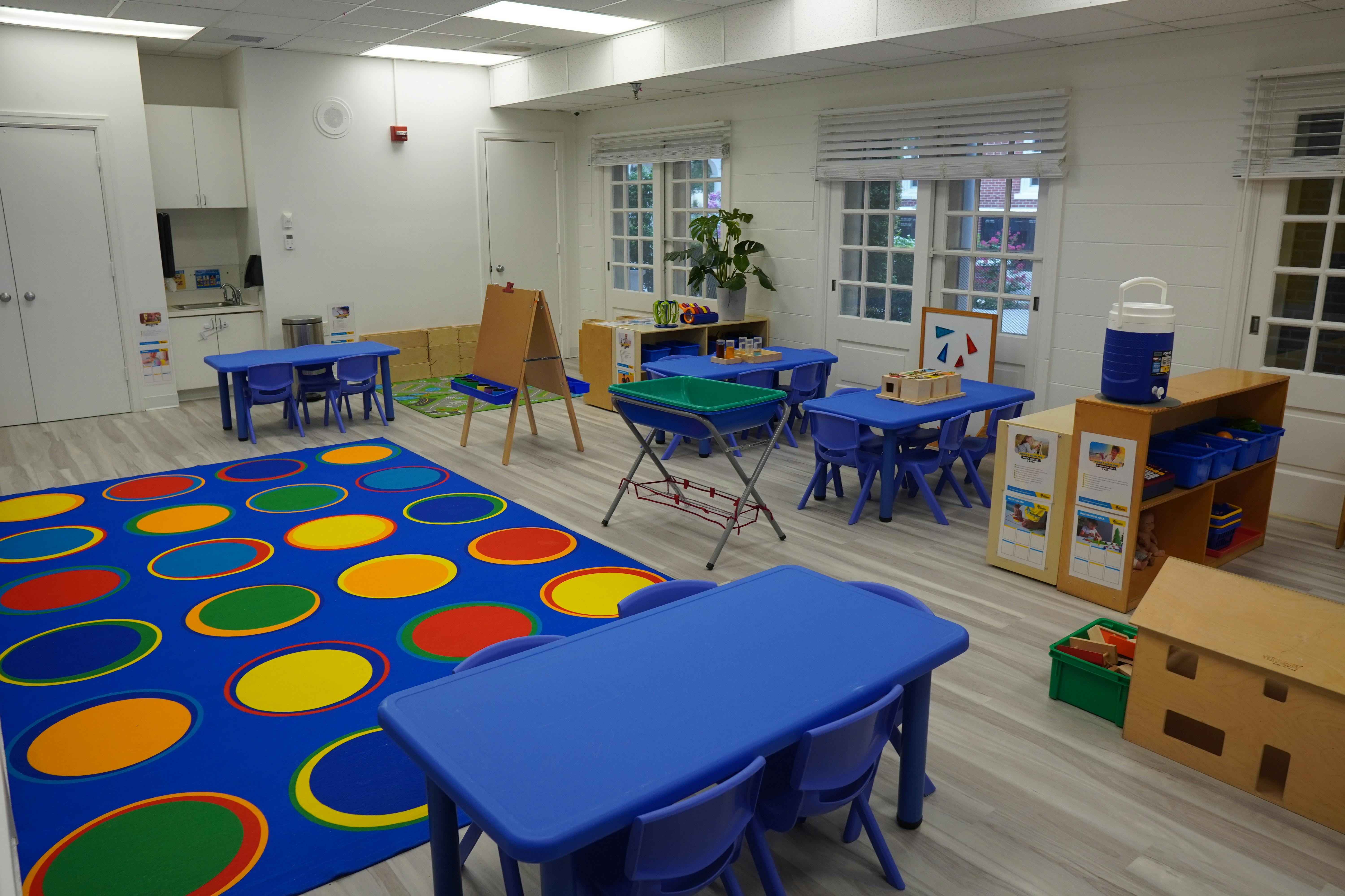 Empty classroom with blue tables and chairs, colorful rug