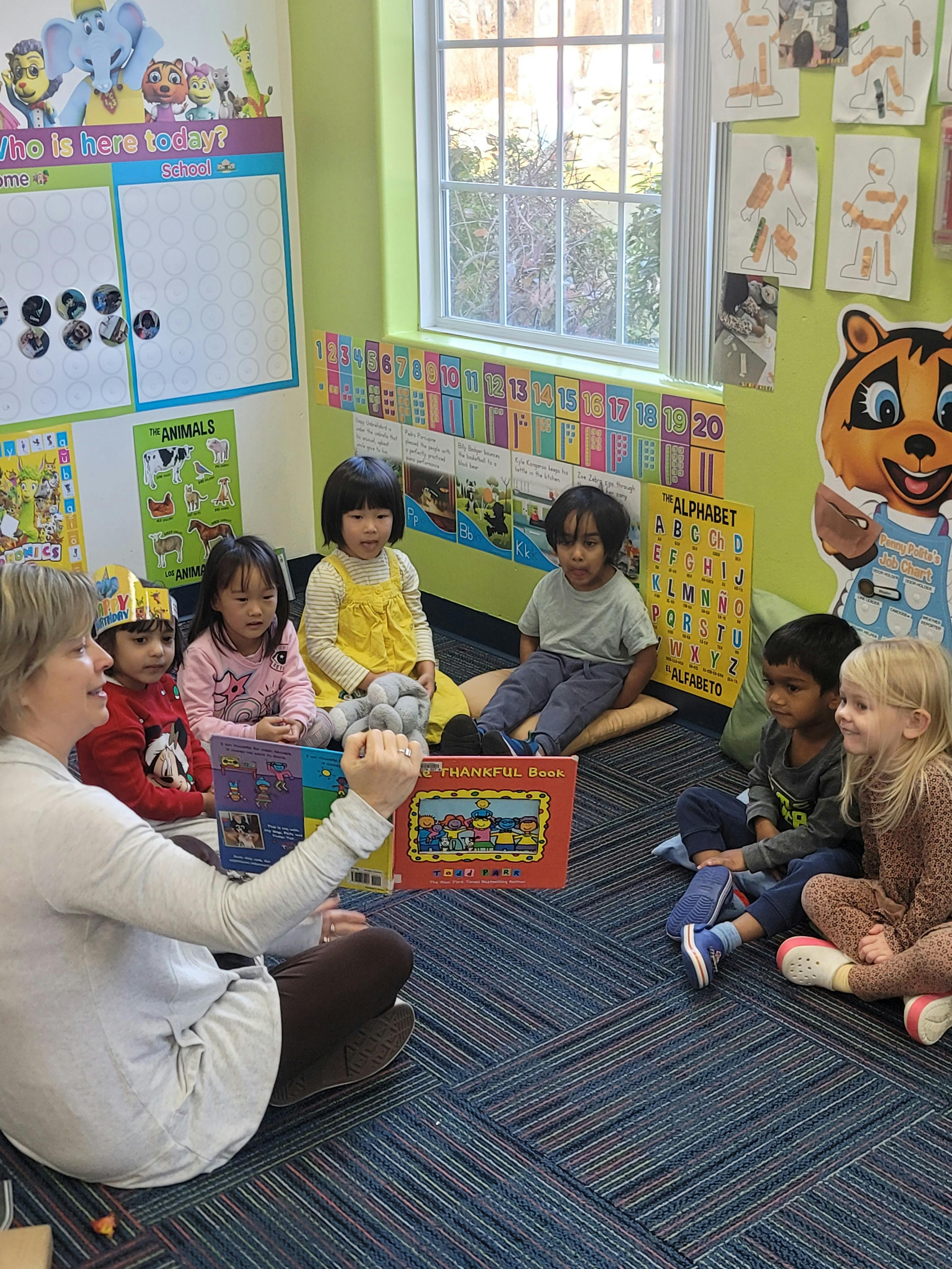 Adult reading a book to a group of children in a classroom
