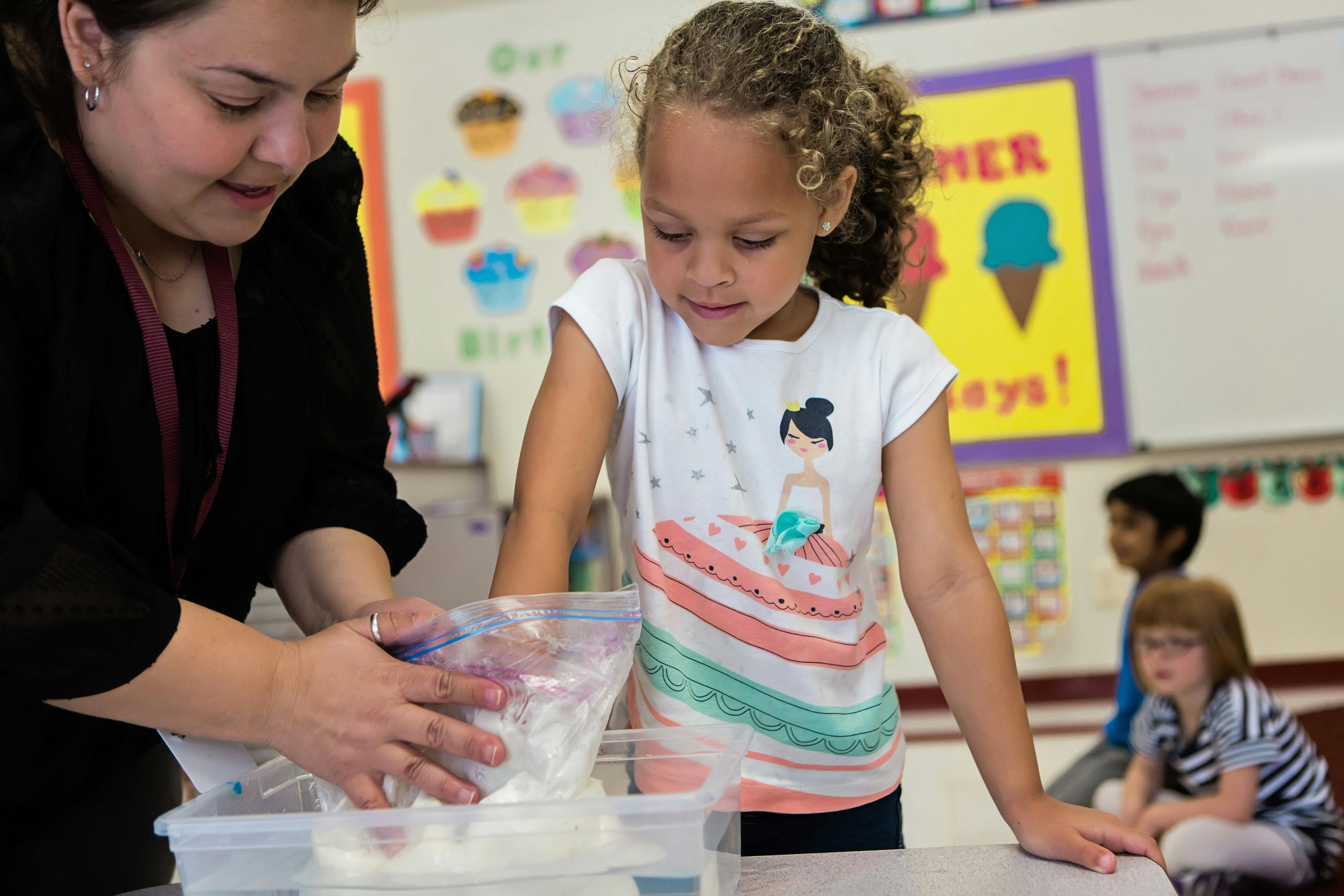 Person and child mixing ingredients in a plastic bag in a classroom