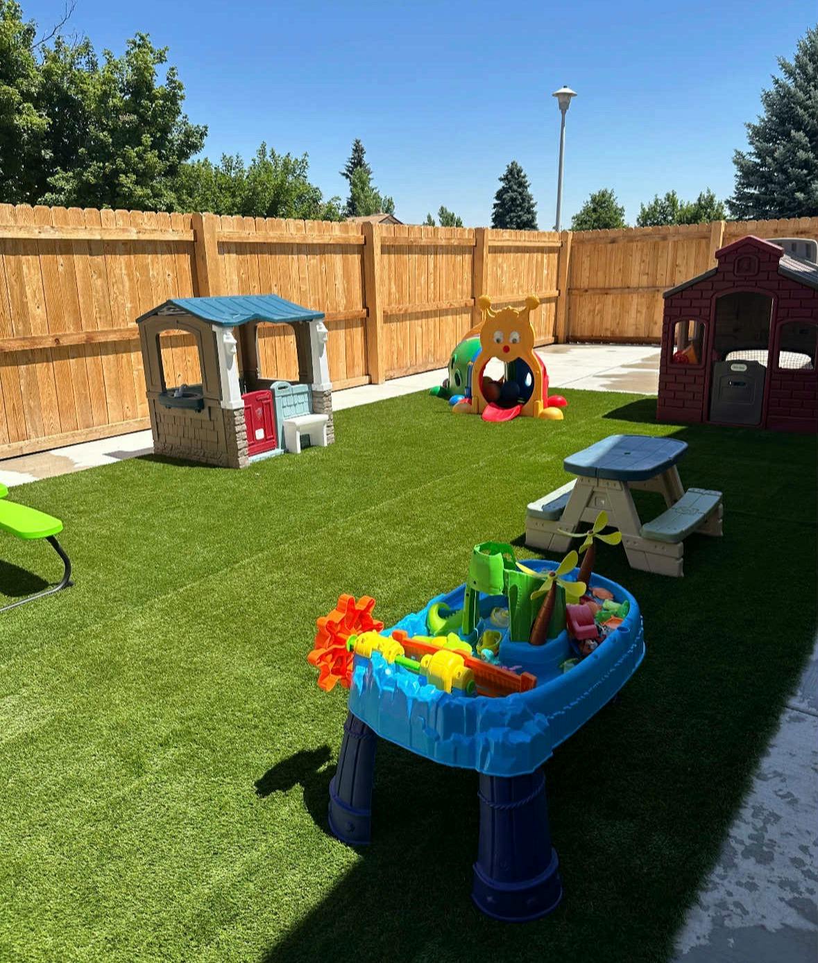 An outdoor play area with artificial turf, playhouses, and a water table