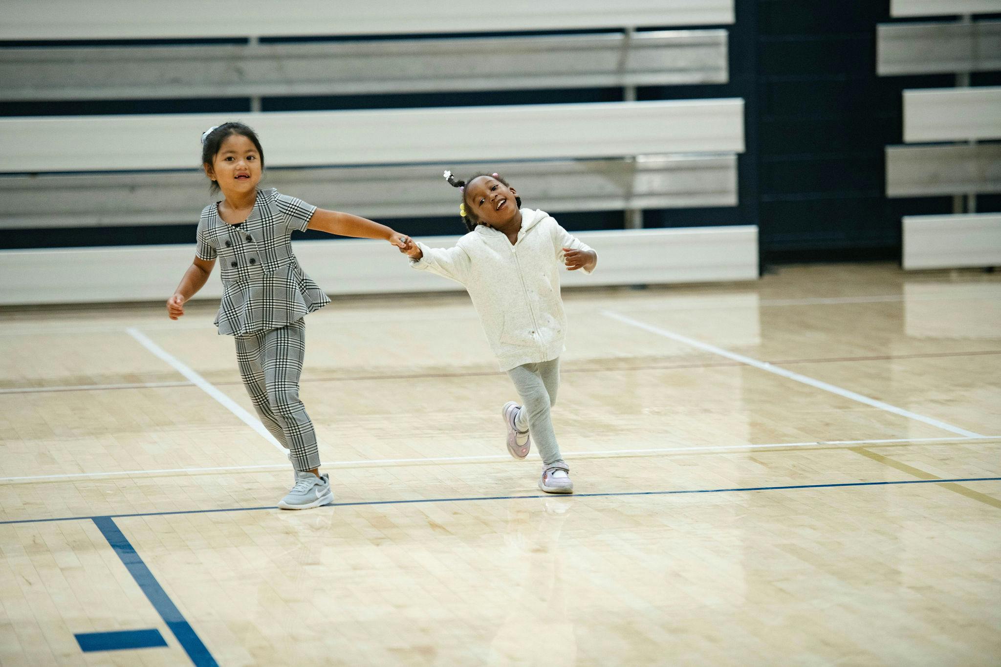 Two children running and holding hands on a gym floor