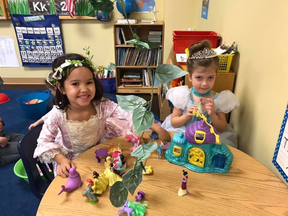 Two children in costumes playing with toys at a table in a classroom