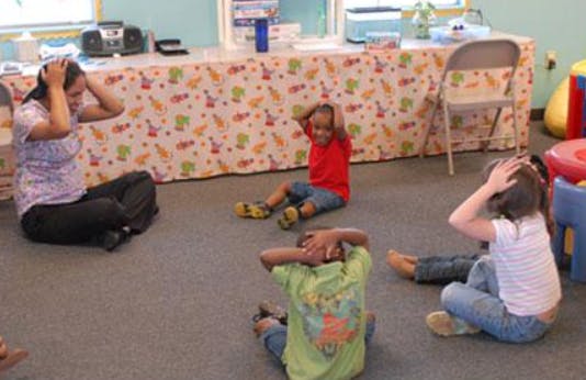 Person and children sitting on floor with hands on heads