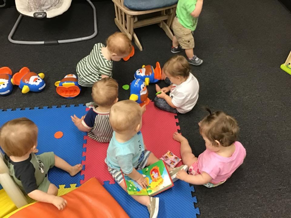 Multiple children playing with toys and books on a colorful mat