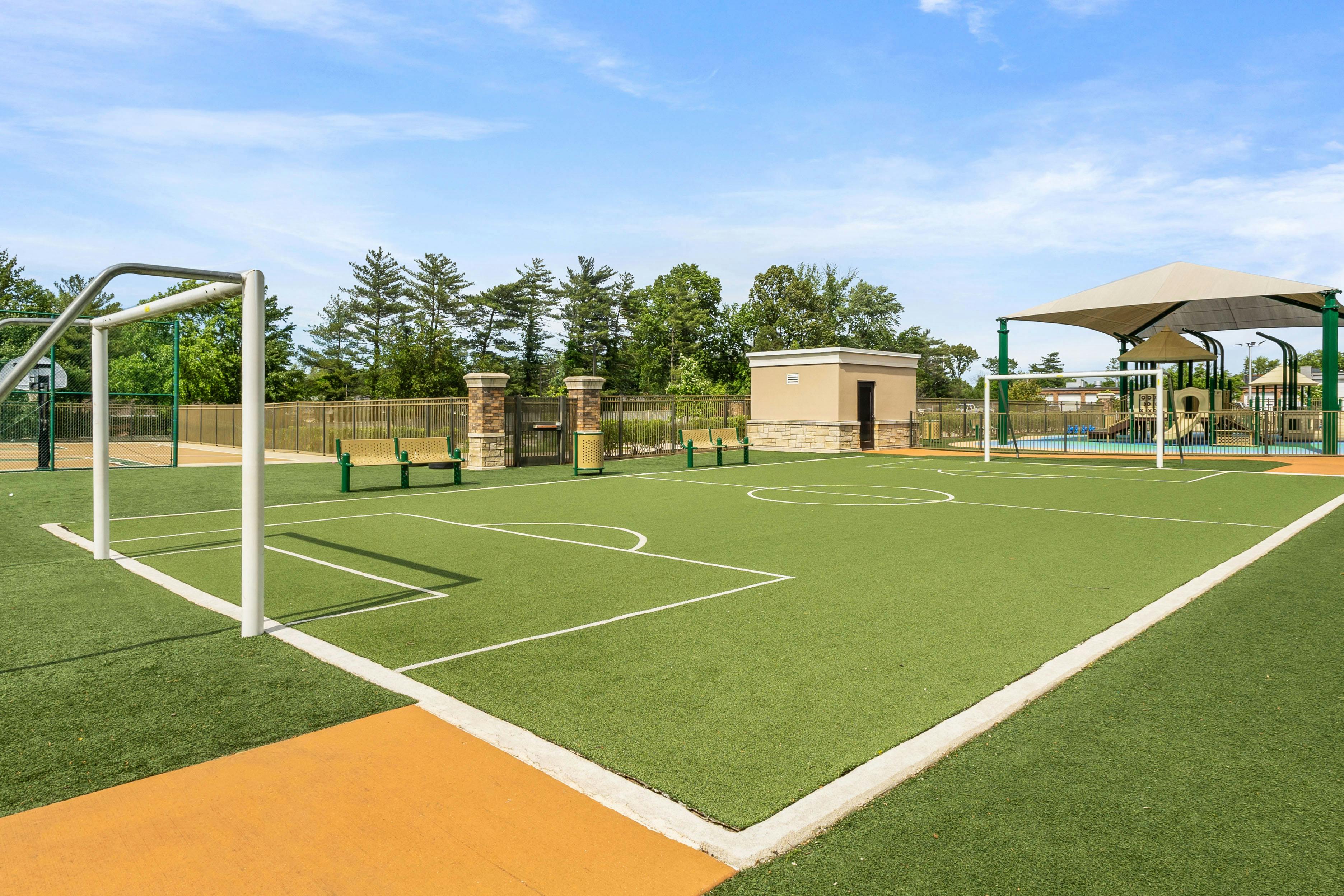 An outdoor turf sports court with a goal, benches, and a small building