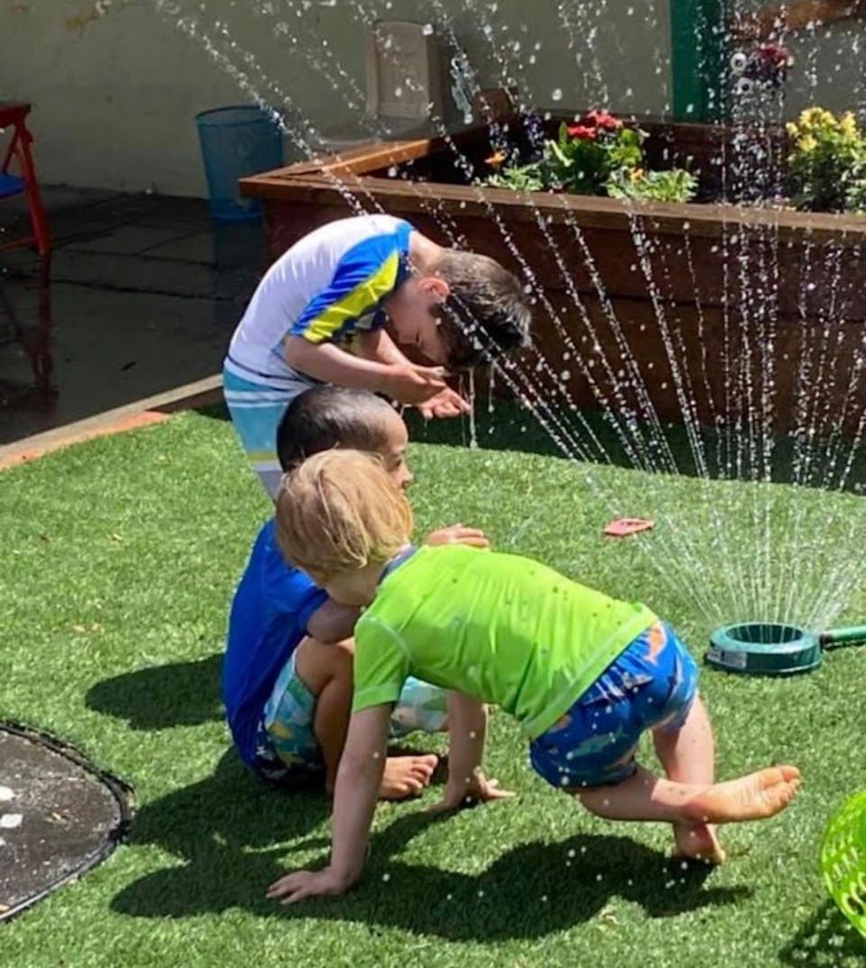 Three children playing in a sprinkler on green turf
