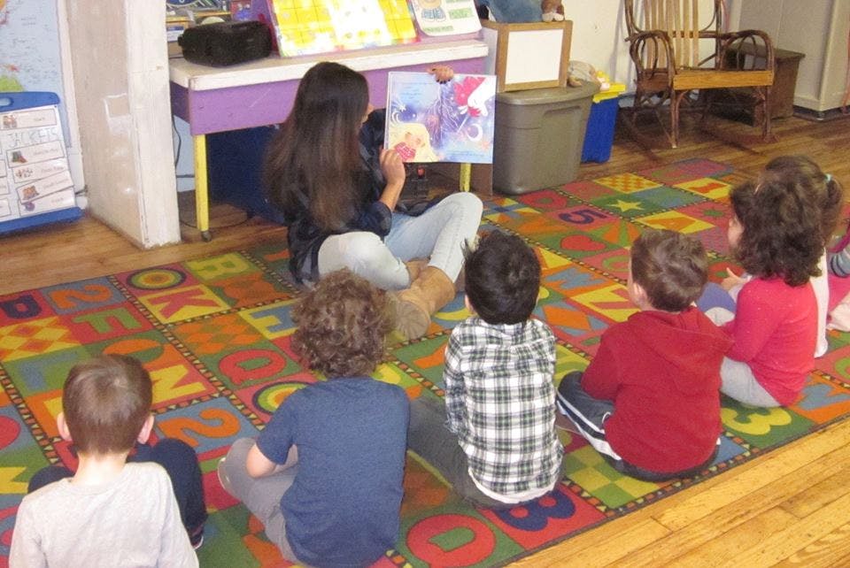 Person reading a book to a group of children in a classroom