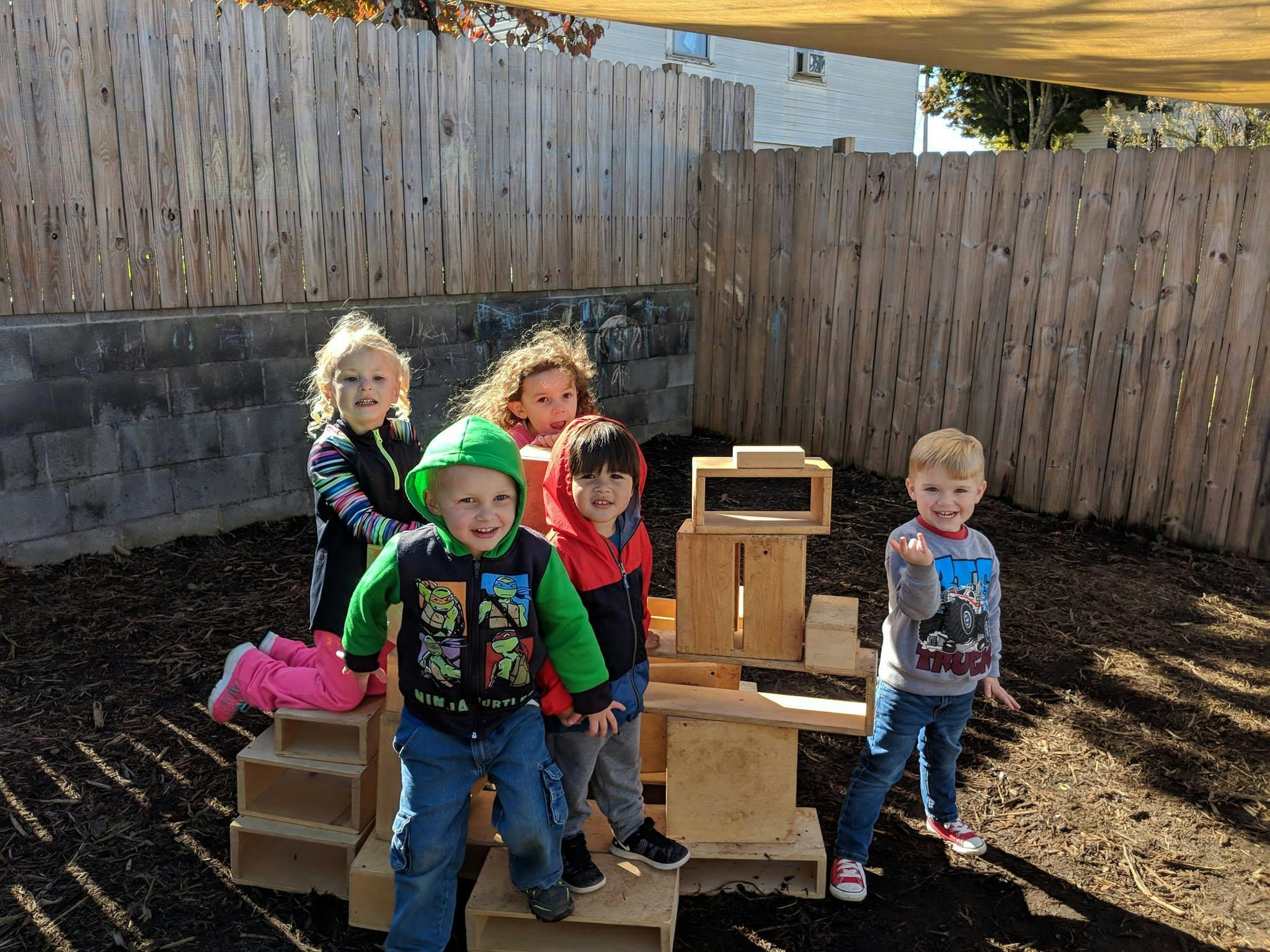 Four children and one teen playing with wooden blocks outdoors