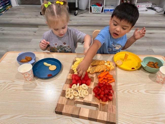 Two children reaching for snacks on a wooden board