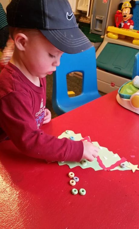 Child in a baseball cap playing with craft materials on a red table