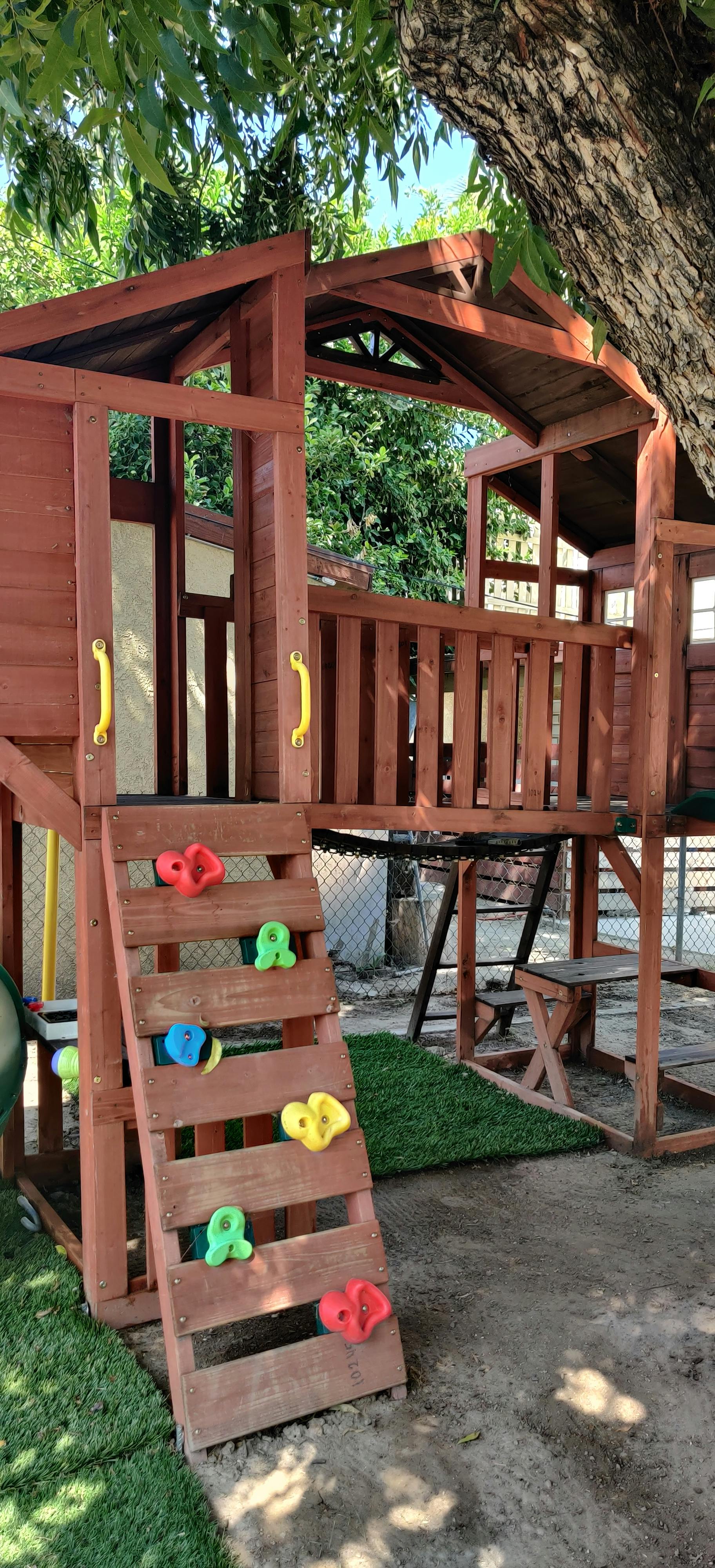 Wooden playground structure with a climbing wall and green turf