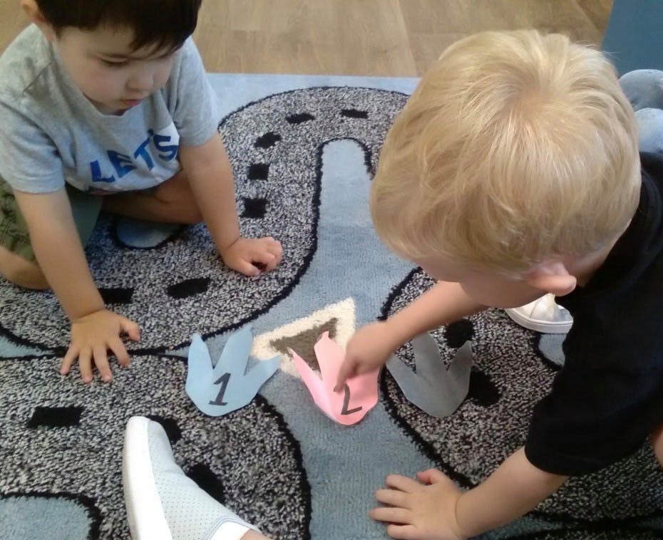 Two children playing with numbered shapes on a rug