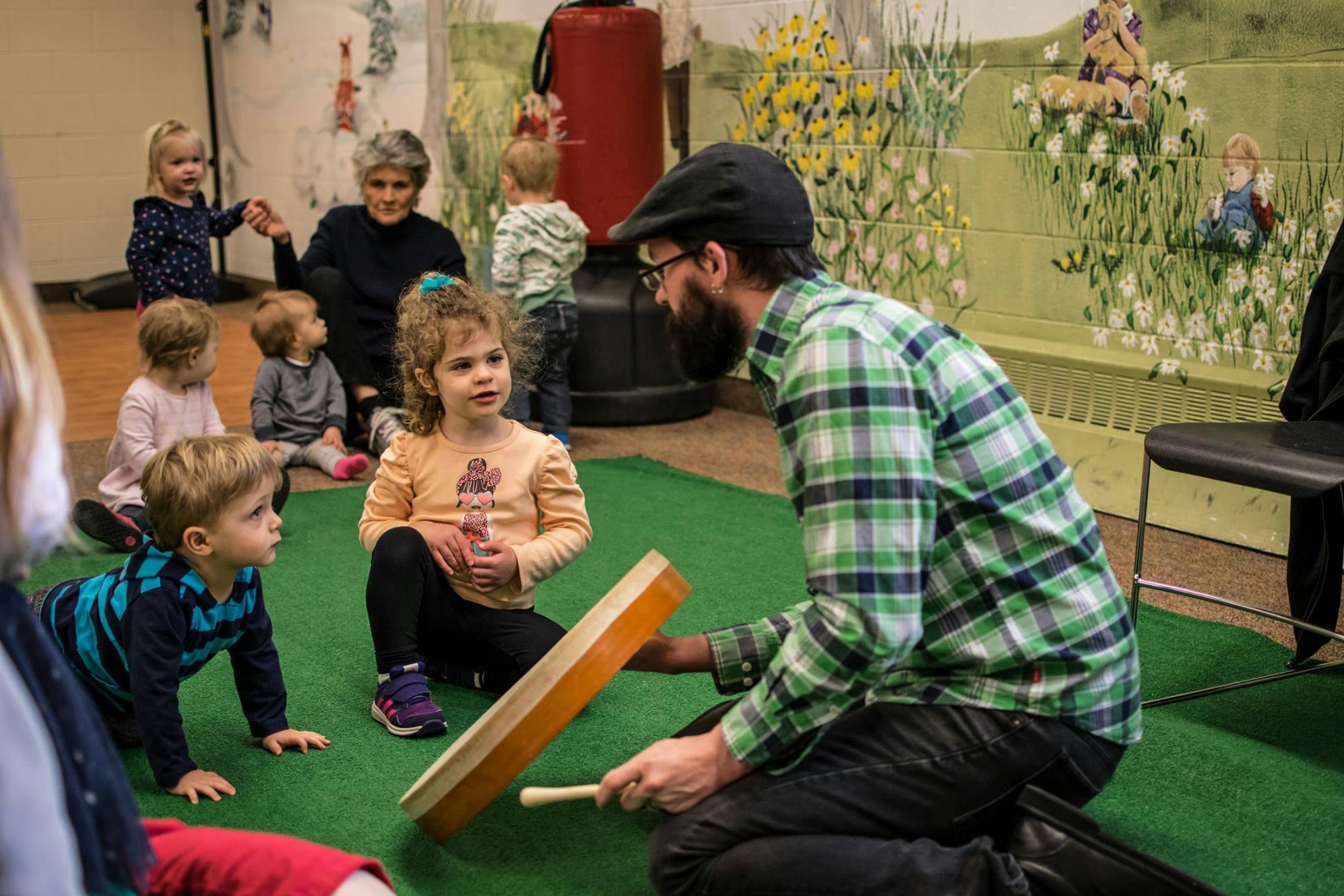 Person playing a drum for children and adults in a room